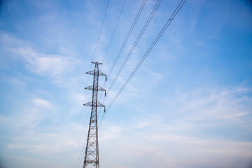 Power lines and electric tower with blue sky and clouds on background.