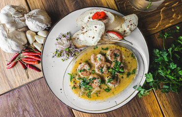 Prawns in spicy sauce served with bread. Top view. White plate on wooden table. Restaurant dish concept. High quality photo