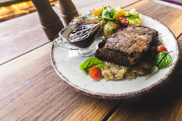 White plate with crispy pork ribs on braised cabbage along with dark sauce and boiled potatoes. Closeup portrait. Indoor shot. High quality photo