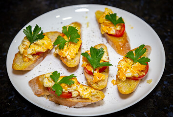 Bread with scrambled egg over ripe tomato and decorated with parsley leaf and black pepper top view