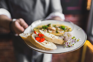 Elegant waiter serving a dish. Plate with bread and shrimps in hot sauce. Blurred background. Restaurant concept. High quality photo