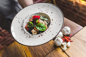 Unrecognizable waiter serving shrimp dish. Black tagliolini pasta with prawns and herbs. Restaurant interior. High quality photo
