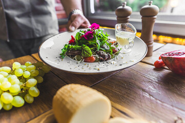 Salad with pieces of duck meat served along with traditional Polish cheese on a white plate by unrecognizable waiter. High quality photo