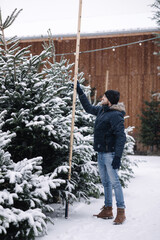 Handsome man measuring Christmas tree outdoor. Man choose fir tree for winter holidays