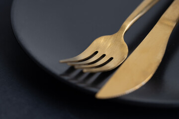 Golden cutlery on plate on dark