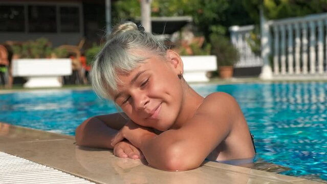 Happy girl is resting in the pool. A younger in swimsuit stay by the pool side in the open air at home in summer. A concept of relax time during vacation period.