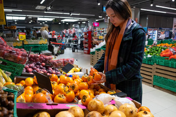 Young latin woman choosing fruits in a grocery store. Persimmon fruit
