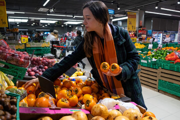 Young latin woman choosing fruits in a grocery store. Persimmon fruit