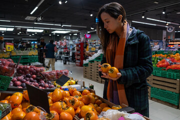 Young latin woman choosing fruits in a grocery store. Persimmon fruit