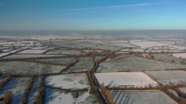 Transverse flight over a patchwork of snowy fields in winter sunshine, blue sky
