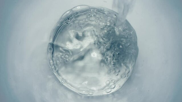 Pure water falling glass closeup. Mineral cool purified aqua swirling in transparent goblet top view. Crystal fresh liquid filling vessel in super slow motion. Sparkling bubbled drink stream