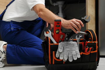 Professional plumber taking adjustable wrench from tool bag indoors, closeup