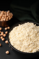 Chickpea flour in bowl and seeds on black table, closeup