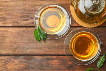 Fresh green tea in glass cups, leaves and teapot on wooden table, flat lay. Space for text