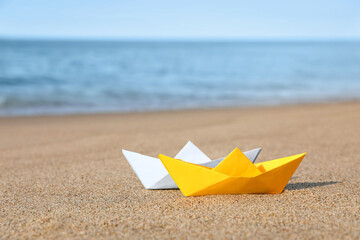 Fototapeta na wymiar Color paper boats near sea on sandy beach
