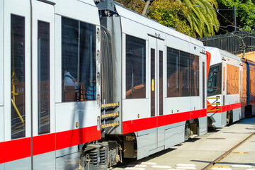 Naklejka premium Tram or downtown train with red and white paint and tinted dark windows with foliage in background and tracks underneath
