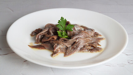 Plate with canned anchovy fillets on white table, closeup