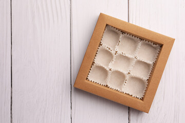 Empty box of chocolate sweets with candy paper cups on white wooden table, top view. Space for text