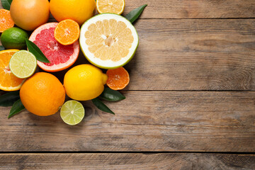 Different ripe citrus fruits with green leaves on wooden table, flat lay. Space for text