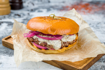 Burger with blue cheese sauce, meat cutlet patty and red onion on grey table