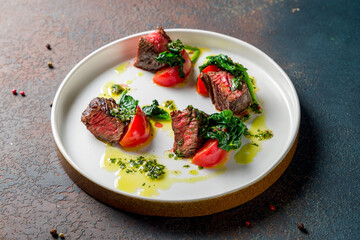 Beef steak sliced with spinach on plate on dark stone table