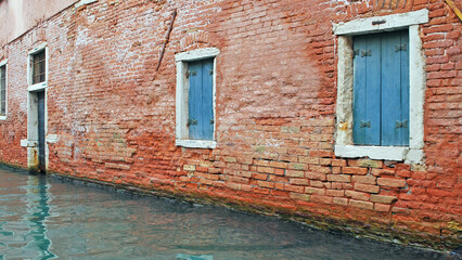 An ancient brick wall with shuttered windows, along one of Venice's famed canals.