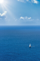 Breathtaking high aerial view of a sailing boat sailing on open sea, beautiful Caribbean ocean, blue skies, white clouds and sunburst