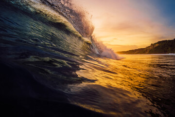 Perfect barrel wave crashing in tropical ocean with warm sunset tones.