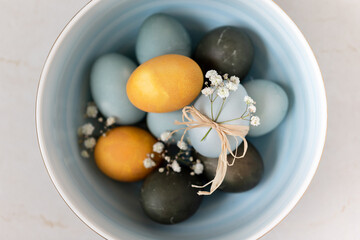 Baby blue, yellow and dark grey Easter eggs in a bowl, top view. Festive decoration.