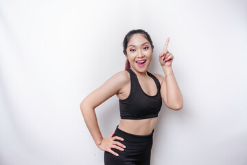 Excited Asian sporty woman wearing sportswear pointing at the copy space on top of her, isolated by white background
