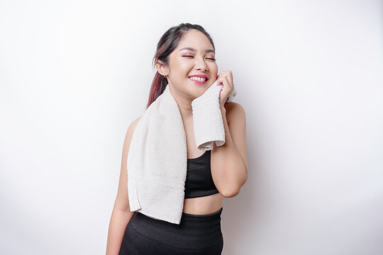 Sportive Asian woman posing with a towel on her shoulder, tired after workout