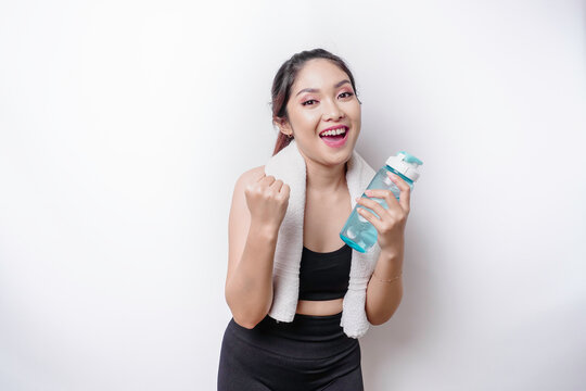 Smiling successful sportive Asian woman posing with a towel on her shoulder and holding a bottle of water