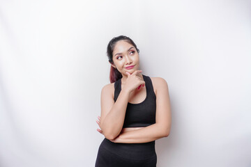 Thoughtful sporty Asian woman wearing sportswear is looking aside while touching her chin, isolated...