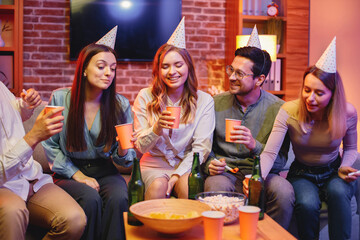 Friends sitting on a sofa in a cozy room and celebrating birthday
