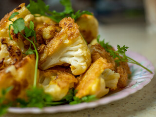 Sprigs of cauliflower baked in batter lying on a white plate, sprigs of fresh herbs are placed on top. Pushing focus, close-up. Selective focus. The concept of cooking healthy vegetable dishes.