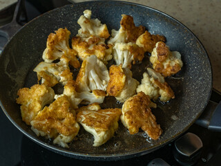 Pieces of cauliflower are fried in vegetable oil in a frying pan. Concept of healthy and wholesome homemade food from vegetables.