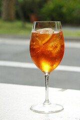 Red cocktail with an orange slice and ice on an outdoor table