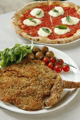 Margherita pizza with tomato sauce, buffalo cheese and basil and Milanese pork cutlet with cherry tomatoes, potatoes and arugula