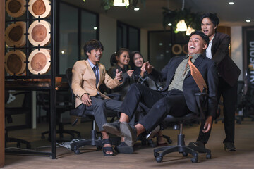 Fototapeta na wymiar Young cheerful business people in suit having fun while racing on office chairs and smiling at the office