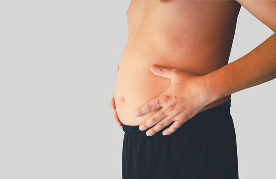 Asian man, obese man standing with his hand rubbing his belly excess fat Fat accumulates in the stomach, big belly