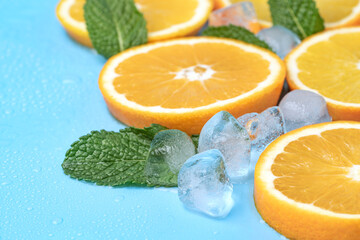 Juicy oranges with ice cubes and mint leaves with copy space on blue background
