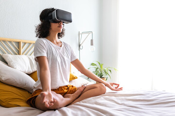 Latina woman meditating with help of VR experience app sitting on bed. Meditation using virtual...