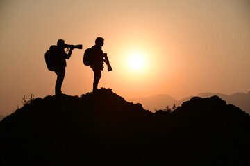 Fototapeta na wymiar Artistic silhouette, Two wildlife photographer taking pictures during sunset from a peak 