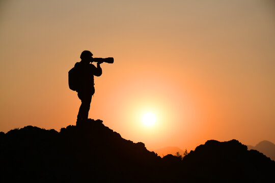 Artistic silhouette, A wildlife photographer taking pictures during sunset from a peak 