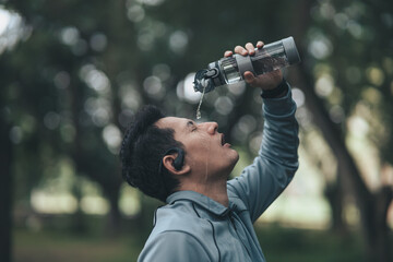 Young sport man drink water after jogging, running in the park. Sport thirsty and resting after exercise..