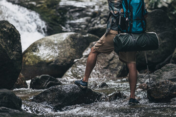 Hikers use trekking pole with backpacks walking through the rock and water on stream in the forest. hiking and adventure concept.