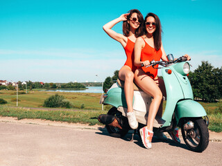 Fototapeta na wymiar Two young beautiful smiling hipster female in summer red bathing suits. Sexy carefree women driving retro motorbike. Positive models having fun, riding classic Italian scooter. In swimwear