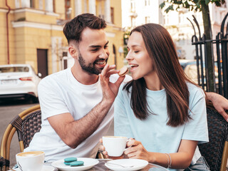Smiling beautiful woman and her handsome boyfriend. Happy cheerful family. Couple drinking coffee in restaurant. They drinking tea at cafe in the street. Holding cup. Feeding his girlfriend