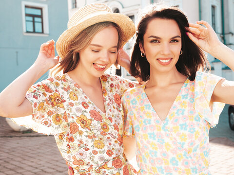 Two young beautiful smiling hipster female in trendy summer white dress clothes and straw hats. Sexy carefree women walking in street. Positive models having fun, hugging and laughing