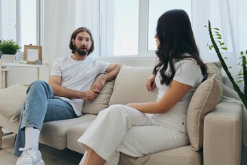 Man and woman friends sitting on the couch and smiling merrily talking to each other having a good time together. Lifestyle in happiness at home